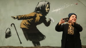 Socially distanced days out woman taking photo next to Banksy picture
